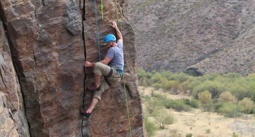 a person climbs a rock wall above green shrubs on an outward bound gap year expedition 